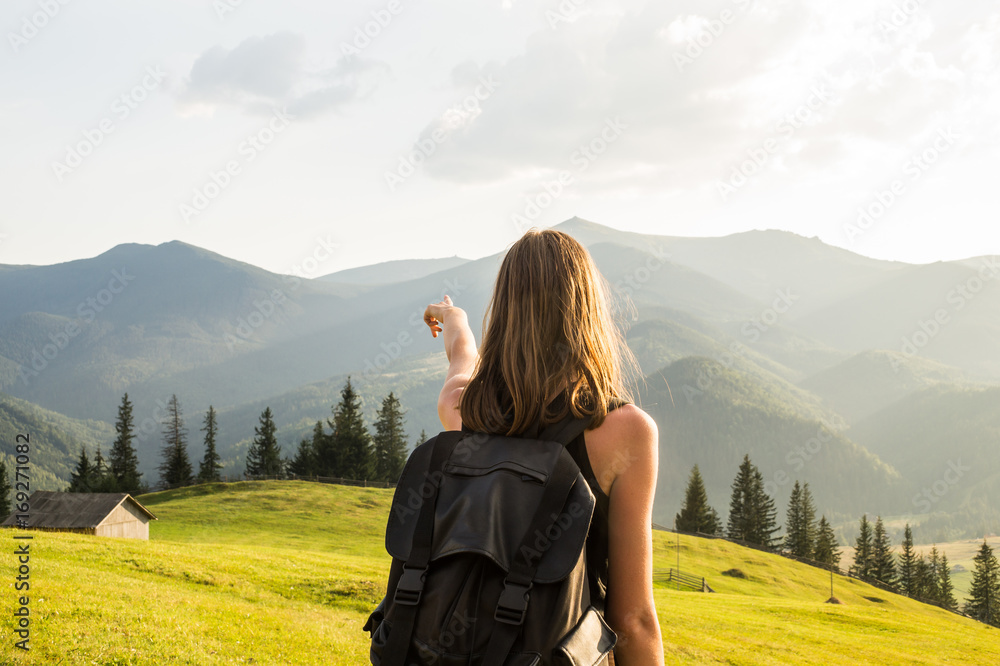Female hiker points to a destination of trip in mountains. Young girl stands at hillside of ukrainian carpathian mountains and looks at distant mountain peaks