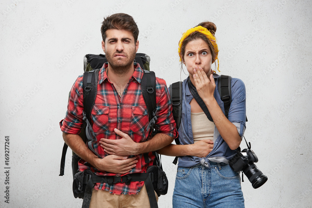Studio shot of bearded young man having painful expression holding