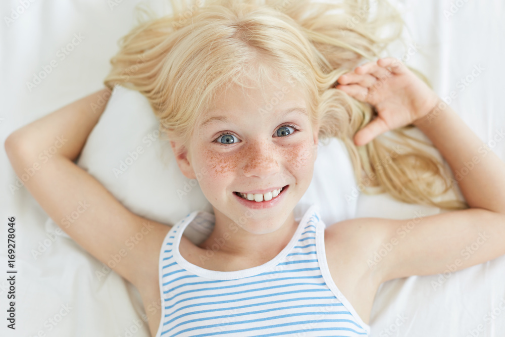 Cute little female child with blonde hair, blue eyes and freckled face,  smiling joyfully while relaxing