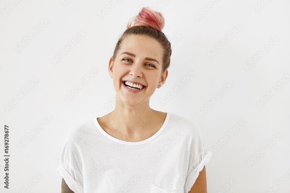 Sincere joy, happiness, youth and carefree life. Indoor shot of lovely hipster girl with hair bun dyed pink having fun, laughing out loud at some joke or funny story, dressed in stylish white t-shirt Sincere joy, happiness, youth and carefree life. Indoor shot of lovely hipster girl with hair bun dyed pink having fun, laughing out loud at some joke or funny story, dressed in stylish white t-shirt