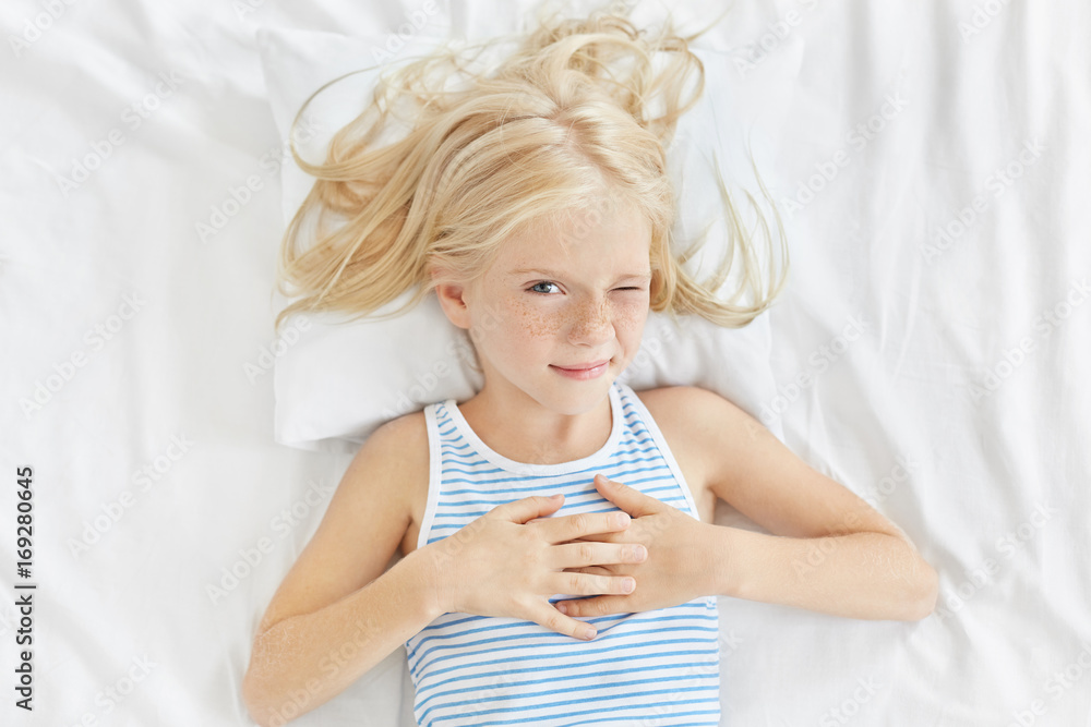 Children, rest and people concept. Lovely little girl with long blonde hair, closing one eye while Children, rest and people concept. Lovely little girl with long blonde hair, closing one eye while