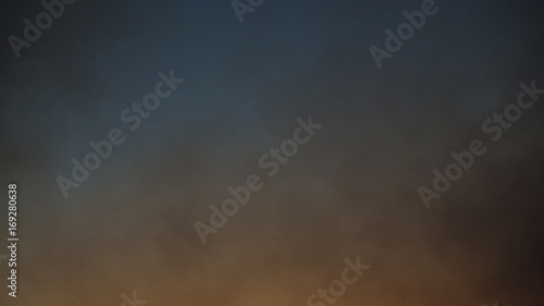Cielo in fiamme durante il tramonto. Nel cielo si espandono nuvole grigie di fumo provenienti dalle fiamme che divampano sulla terra e che danno quel colore arancione in basso. photo