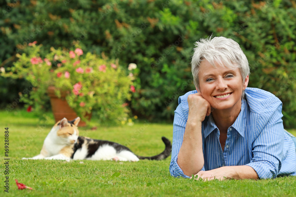 Attraktive Seniorin liegt im Gras mit Katze im Hintergrund Attraktive Seniorin liegt im Gras mit Katze im Hintergrund