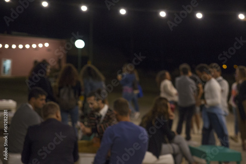 Persone sfocate durante una festa che bevono e mangiano mentre fanno chiacchiere. L' evento si svolge in un agriturismo all' aperto di notte.