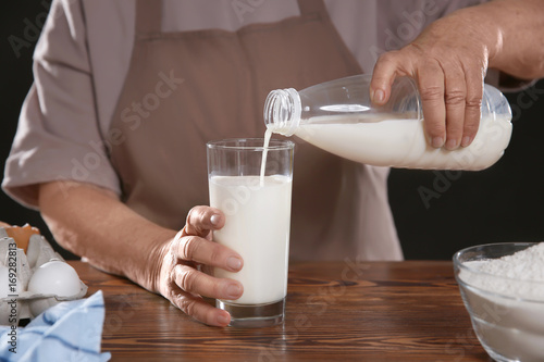 Old woman pouring fresh milk into glass on table