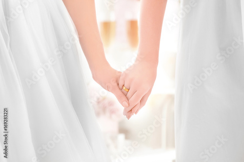 Young lesbian brides holding hands on light background