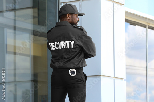 Fototapeta Male security guard standing near big modern building