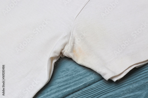 T-shirt with sweat stain on wooden background. Concept of using deodorant