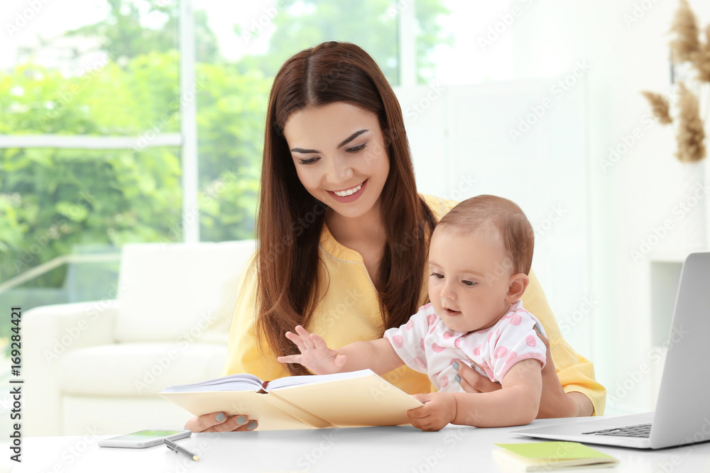 Young mother holding baby while working in home office Young mother holding baby while working in home office
