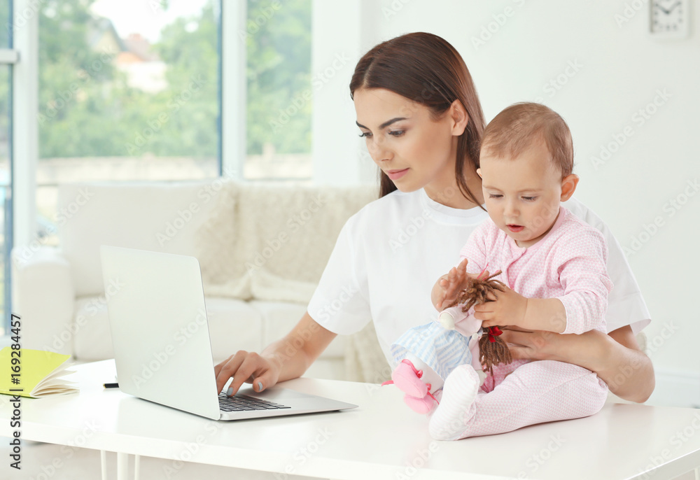 Young mother holding baby while working in home office Young mother holding baby while working in home office