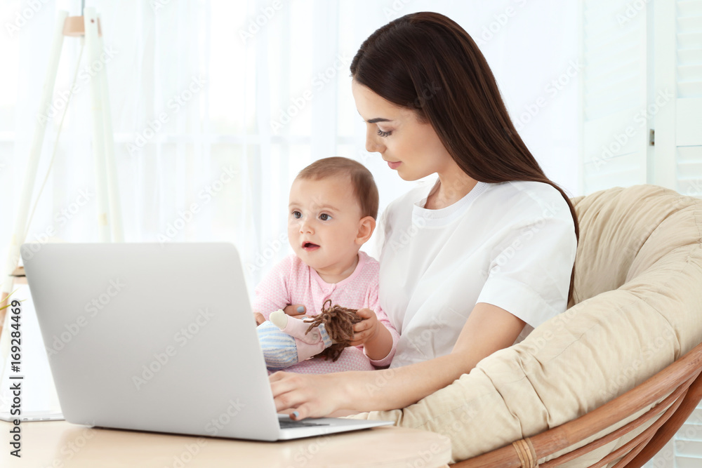 Young mother holding baby while working in home office Young mother holding baby while working in home office