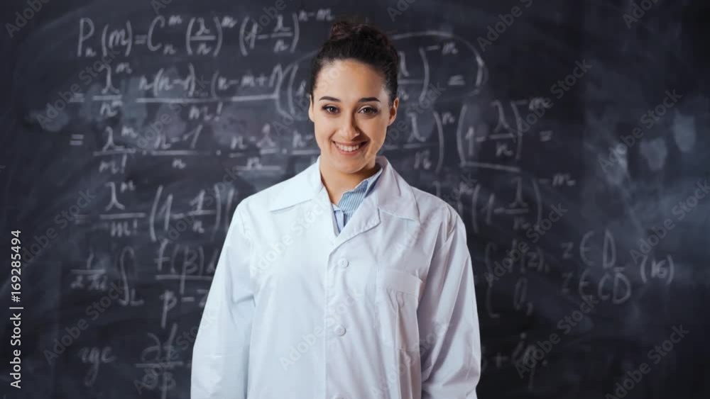 Young student female in white robe solve hard and heavy to understand math equation on black chalk board, She turn to camera and smile. Smart, clever, intelligent scientist woman concept. Young student female in white robe solve hard and heavy to understand math equation on black chalk board, She turn to camera and smile. Smart, clever, intelligent scientist woman concept.