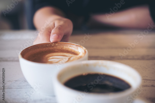 Close up image of two people clink white coffee mugs on wooden table in cafe