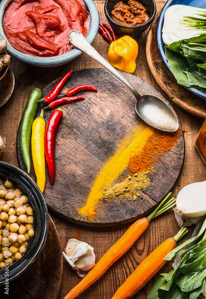 Indian vegetarian cooking ingredients with colorful ground spices , indian curry paste, chick peas  , vegetables and spoon on wooden background, top view, frame.  Healthy food and eating  concept