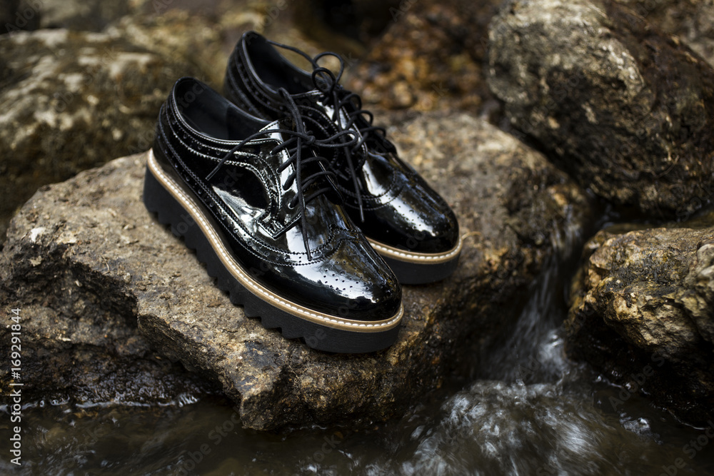 Black shiny patent leather women's brogues shoes on old gray stones, near  river in a forest or park. Fashion advertising shoes photos. Stock Photo |  Adobe Stock