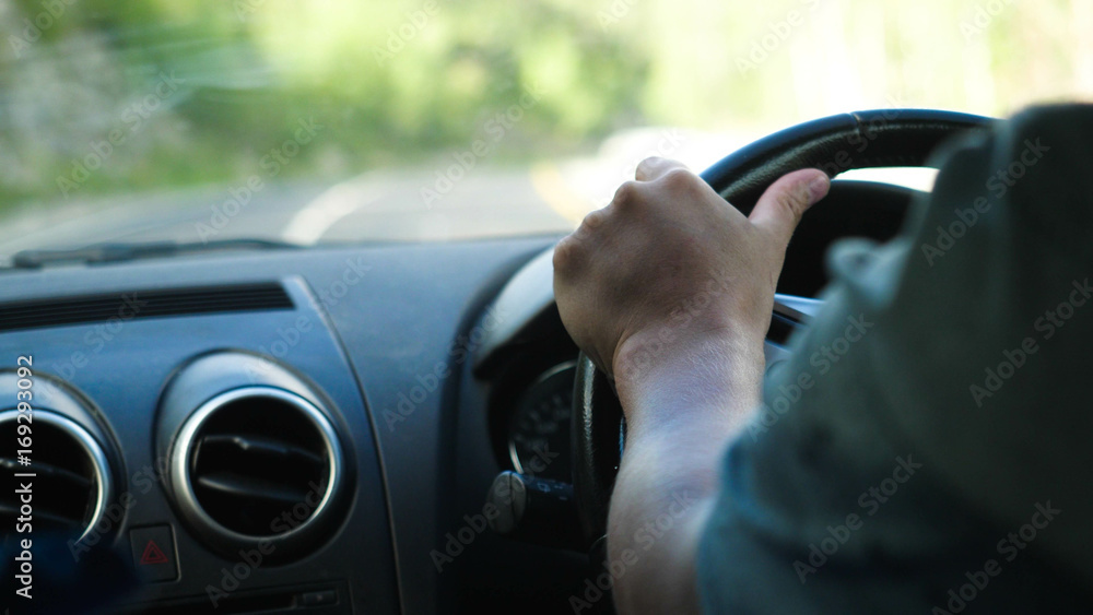 Close up of male hand on the steering wheel driving a car in the long road along mountains Close up of male hand on the steering wheel driving a car in the long road along mountains