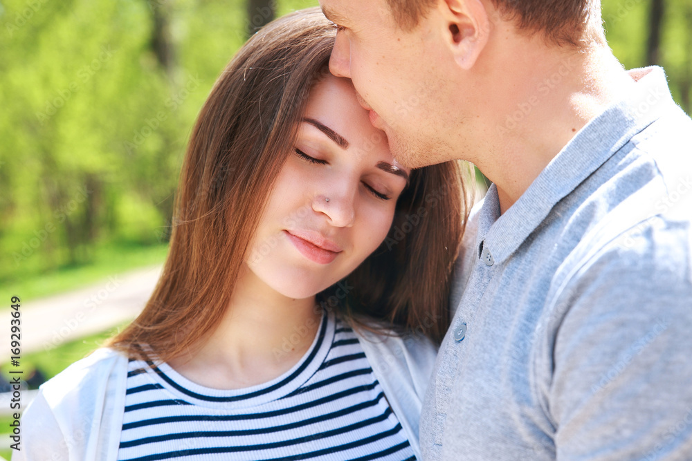 Handsome man and his beautiful pregnant wife are hugging and smiling while standing in park Handsome man and his beautiful pregnant wife are hugging and smiling while standing in park