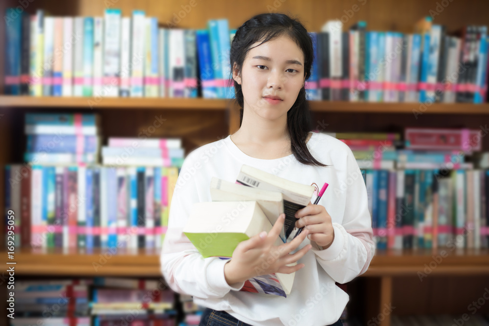 Asian female students holding for selection Book  in library