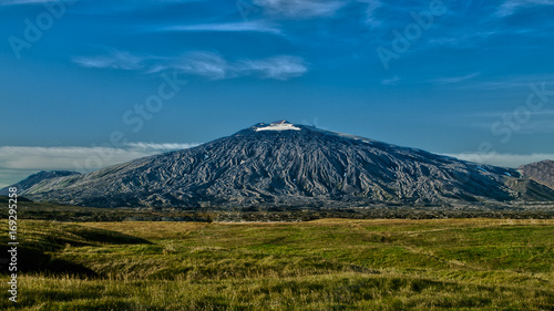 Obraz na płótnie Panoramic view of black volcano Snæfellsjökull with blue sky above and green dry grass below . West Iceland, Europe. w salonie
