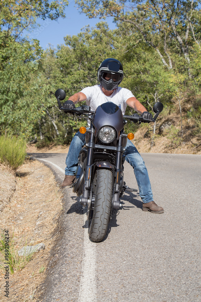 Obraz premium Front view of man sitting on parked custom motorcycle on road in mountains. 