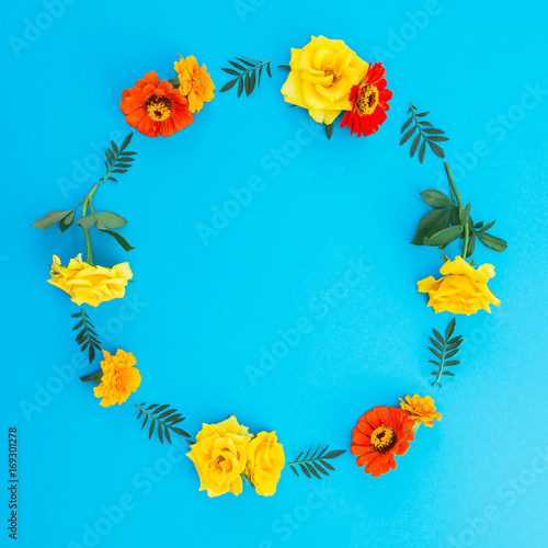 Round frame of flowers on blue background. Flat lay, top view. Floral background.