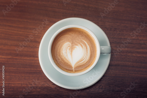 Top view of hot cappuccino with latte art in pastel blue cup on dark brown wood table near window in morning,vintage filtered,