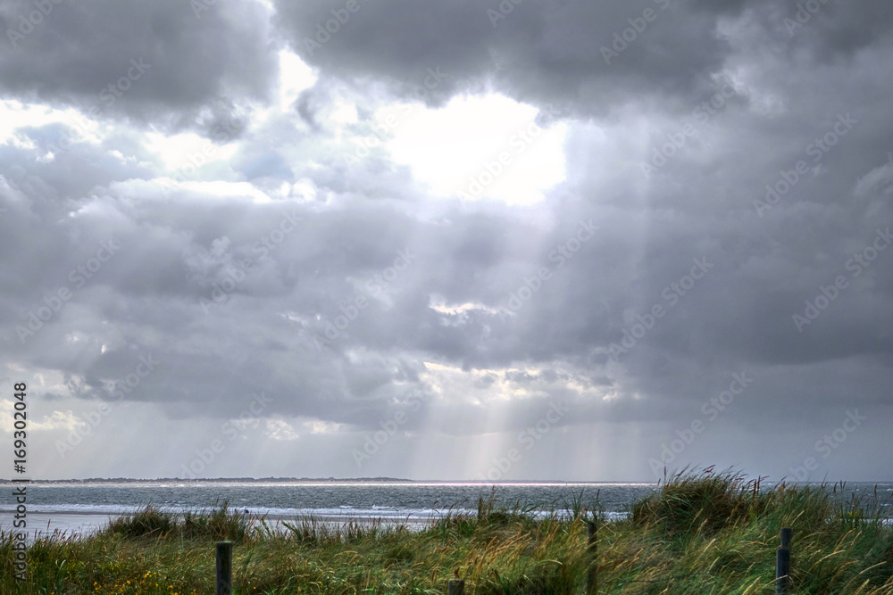 Sonnenstrahlen brechen durch Regenwolken am Meer