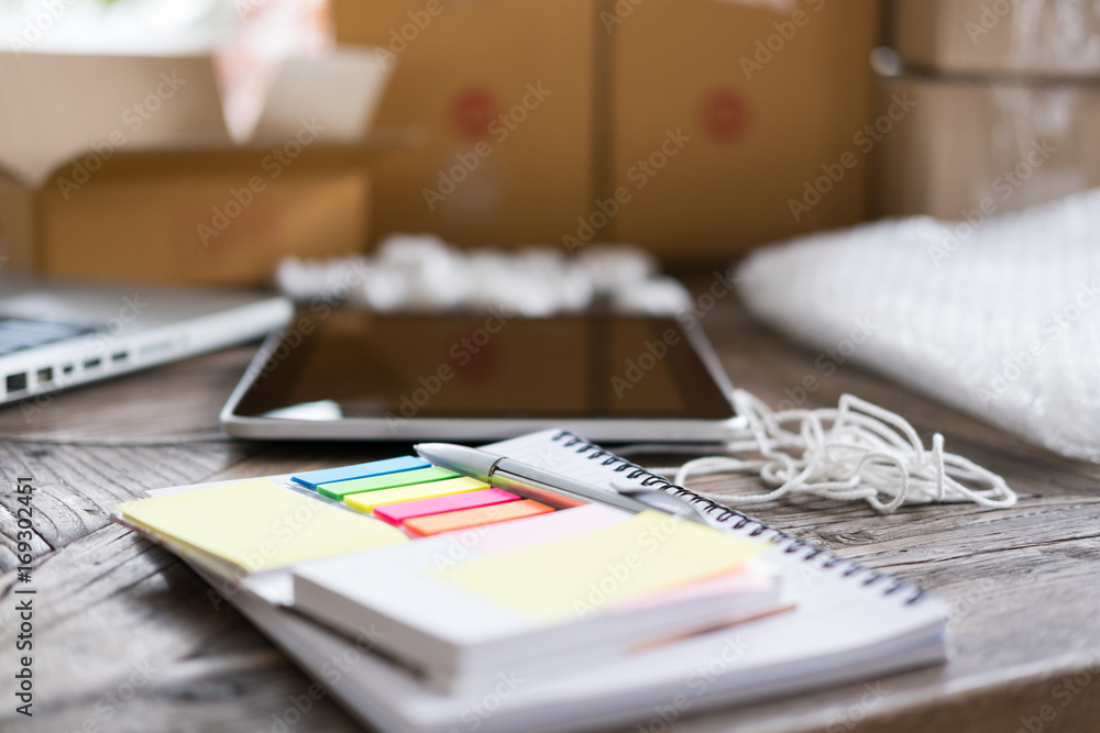 notebook, pen at workplace of business owner, freelance, entrepreneur, SME seller. cardboard parcel box of product for deliver to customer. Online selling, e-commerce, packing, shipping concept notebook, pen at workplace of business owner, freelance, entrepreneur, SME seller. cardboard parcel box of product for deliver to customer. Online selling, e-commerce, packing, shipping concept