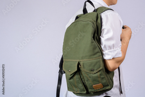 Student with small backpack on grey background.
