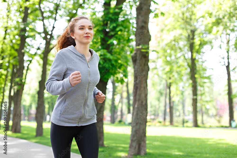 Young woman jogging in green park, copy space Young woman jogging in green park, copy space