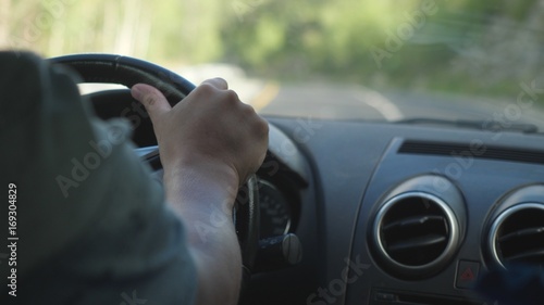 Close up of man's hand on the steering wheel driving a car in the long road along mountains