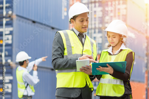 Asian Businessman , Asian secretary and Asian Container inspector working in yard with communication device walkie talkie communicate report number checking container.