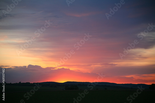 Natural Sunset Sunrise Over Field Or Meadow. Bright Dramatic Sky And Dark Ground. Countryside Landscape Under Scenic Colorful Sky At Sunset Dawn Sunrise. Sun Over Skyline, Horizon. Warm Colours. © stozubanatoly