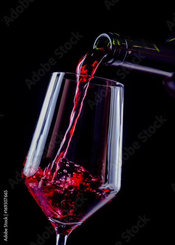 Red wine pouring in wineglass from a bottle on black background. Wine list design menu with copyspace.