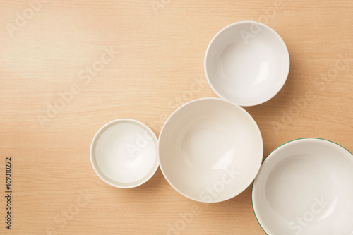Four empty bowls on light wood background  Flat top view