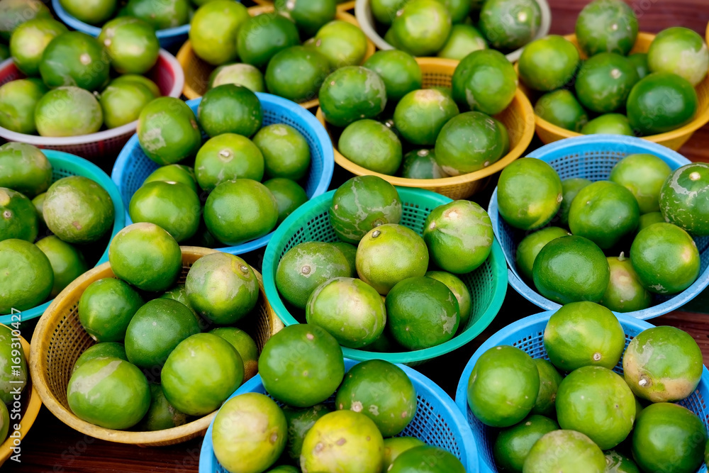 Stack of Green local lemons in plastic baskets on wood table for sell in the market. Stack of Green local lemons in plastic baskets on wood table for sell in the market.