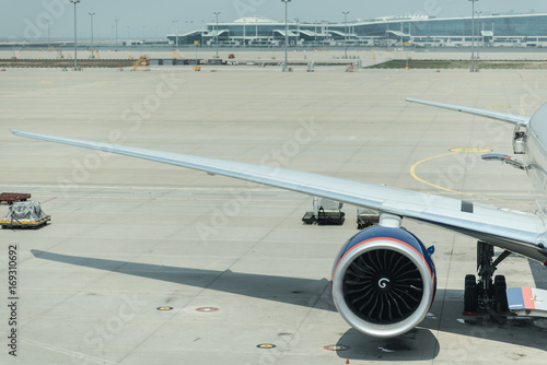 Passenger wide-body plane on the airport runaway. Motor and wing close up. Pre-flight service of airplane. Boarding bridge docked with aircraft. photo