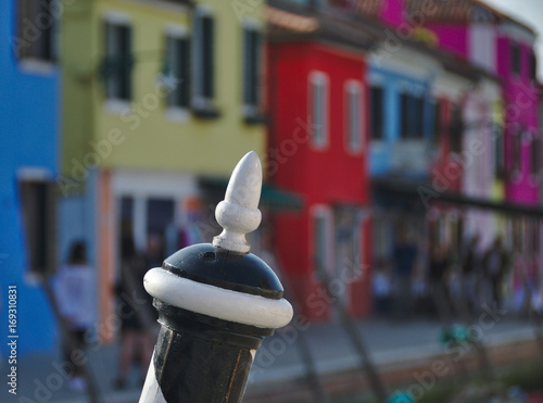 Close-up of typical striped wooden boat mooring post tip with colorful houses in background in Burano island near Venice, Italy