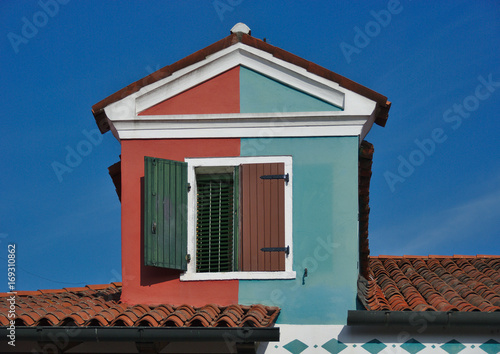 Two-colored tiled mansard roof gable dormer window with blinds in Burano island, Italy