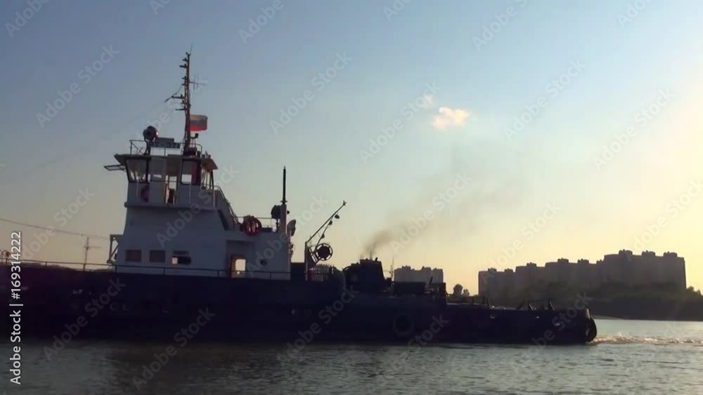 A powerful slow-moving tug pushes a barge with a cargo to the port of unloading along a wide river at sunset A powerful slow-moving tug pushes a barge with a cargo to the port of unloading along a wide river at sunset