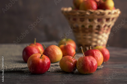 Small red apples Ranetki on a wooden table with a wicker basket. Still life with apples.