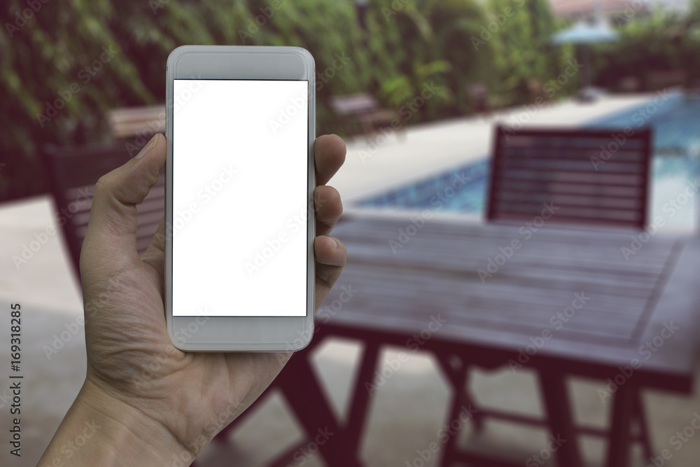 Hand holding smartphone with white blank screen over blurred Lounge table by the pool background for product display montage Hand holding smartphone with white blank screen over blurred Lounge table by the pool background for product display montage