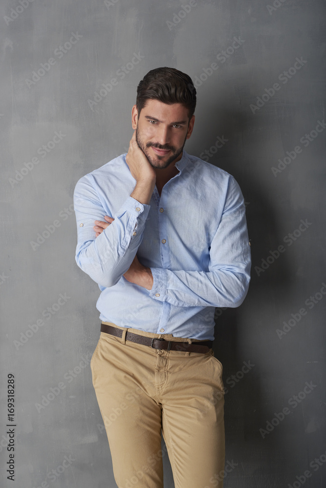 Confident young man standing at grey wall in the studio.