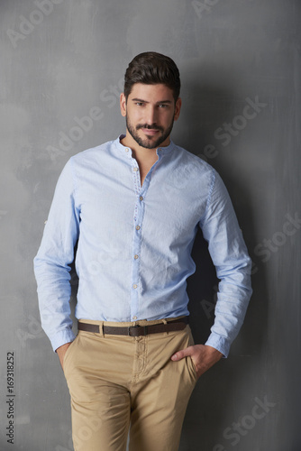 Confident young man standing at grey wall in the studio.