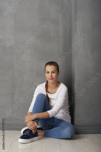 Full length studio shot of a happy young woman sitting at grey wall with copy space.