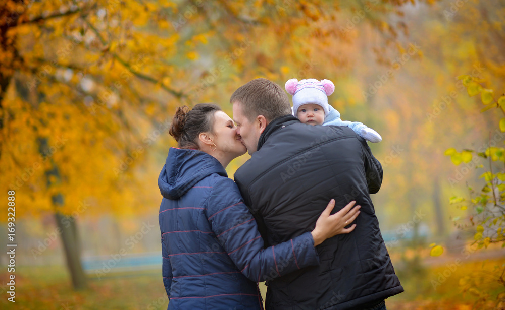happy family walks in the autumn park, the father holds the kid on hands and kisses mother