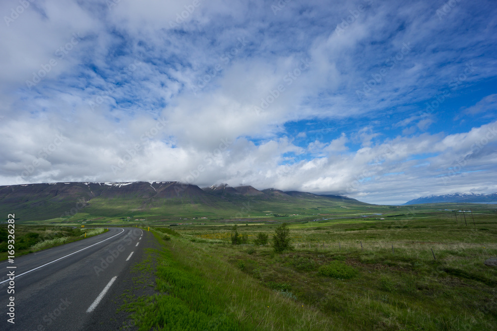 Iceland - Green moss covered volcanoes with snow covered tops behind road bend