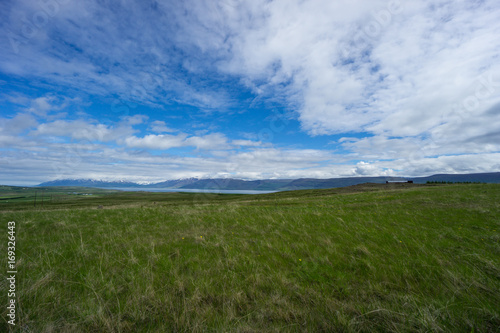 Iceland - Wide green open range with fjord before snowy mountains at blue sky
