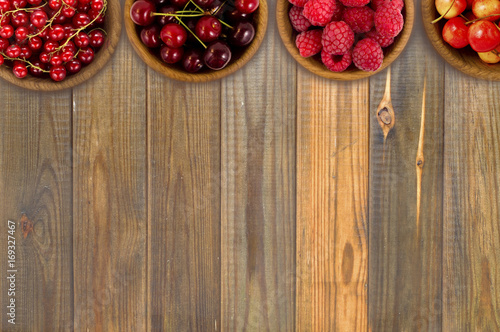 Red berries at border of image with copy space for text. Raspberry, strawberry, pomegranate, currant in a wooden bowls. Top view.