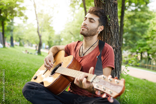 Hipster guy with beard having joyful look, singing songs, enjoying free time at the park. Positive emotions.